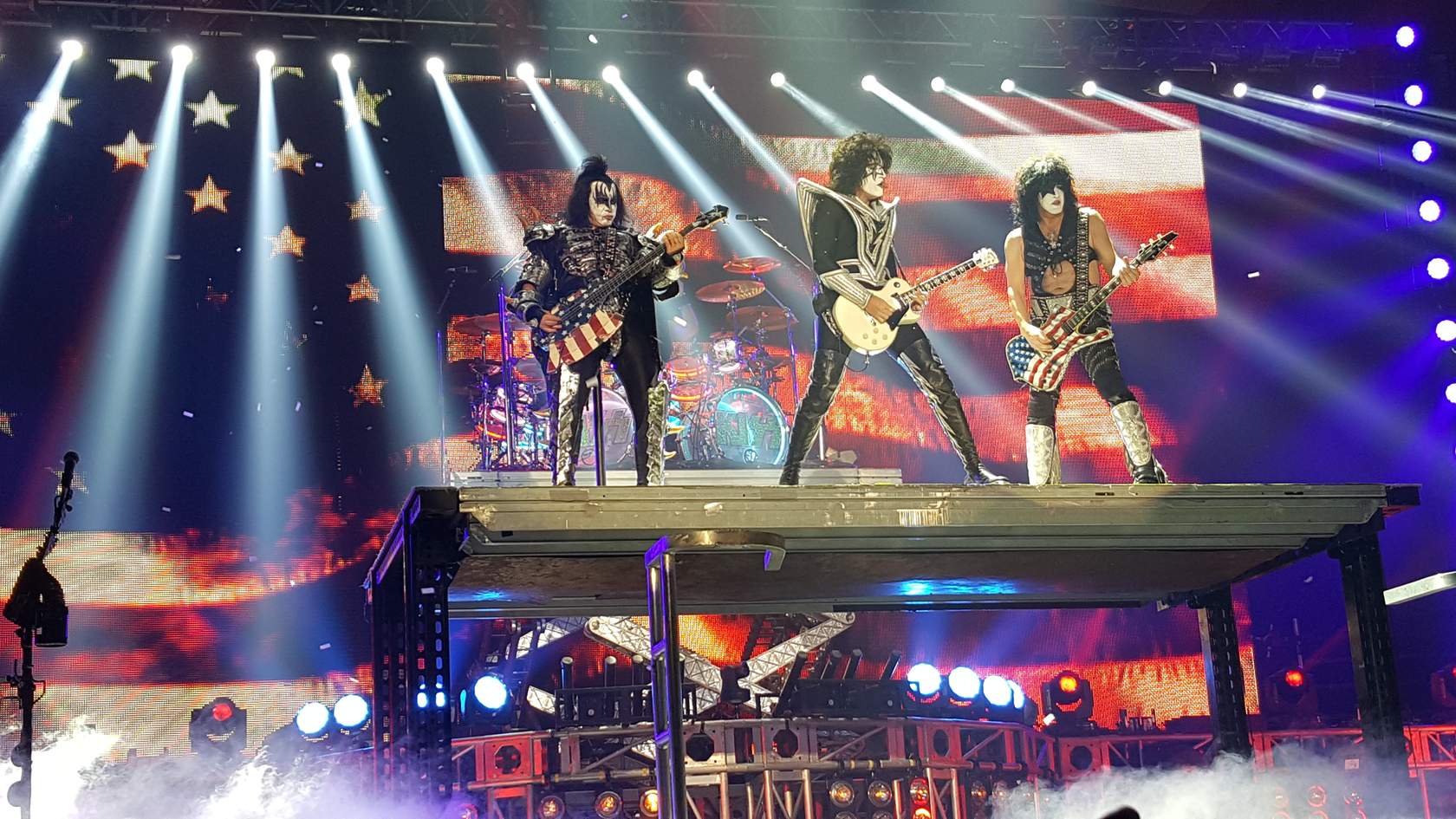 Kiss performs on stage in front of a patriotic flag, showcasing their relational framing.
