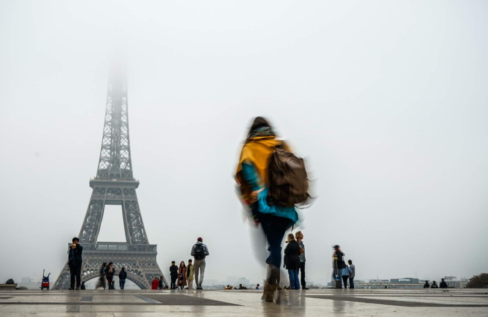A woman walks past the Eiffel Tower on a foggy day in Paris, capturing RFT0707.