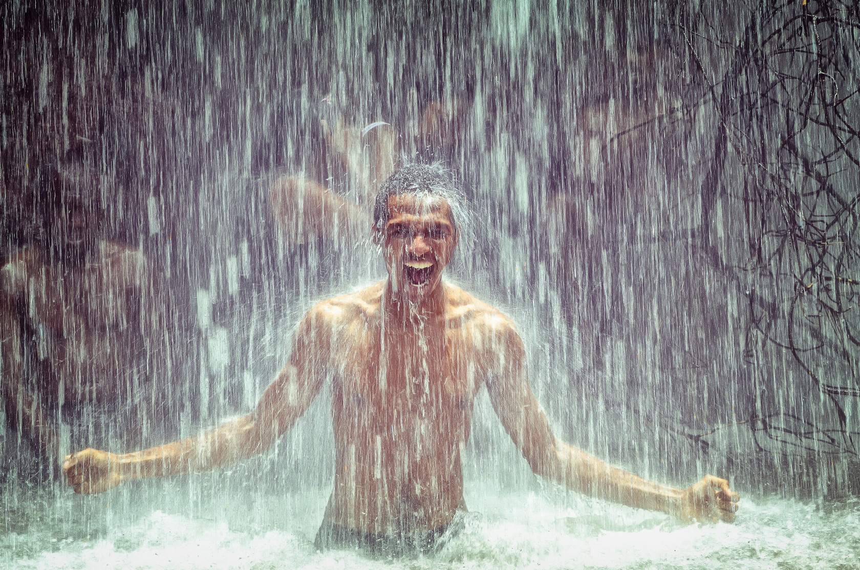 A man is standing under a waterfall with his arms open, showcasing the product.