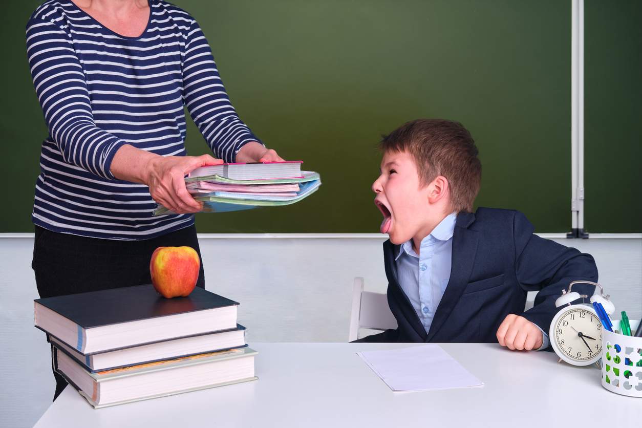 A teacher is fluently handing a boy a stack of books with flexibility.